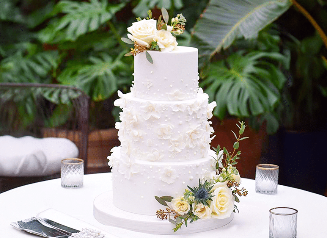 Cake designer adding fresh flowers to a three-tier wedding cake at a Friendswood, TX lakeside pavilion
